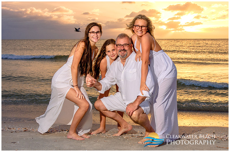 photo of father and daughters in front of sunset on sand key beach